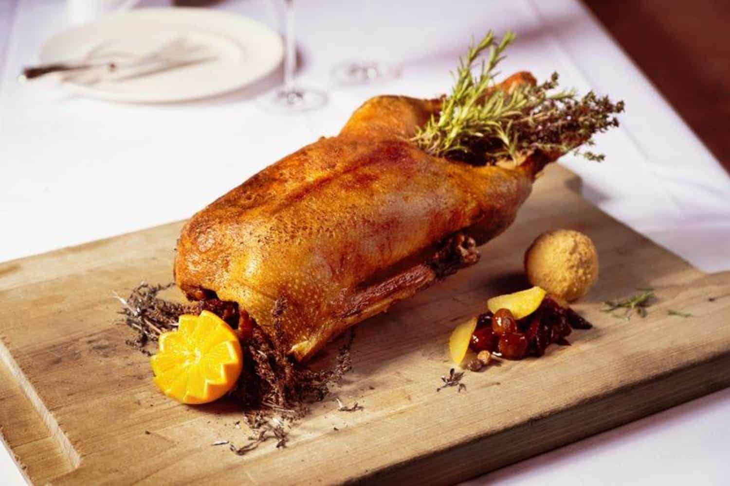 Eine gebackene Ente gefüllt mit Rosmarin liegend auf einem Holzbrett im Gourmetrestaurant Hanse Stube in Köln